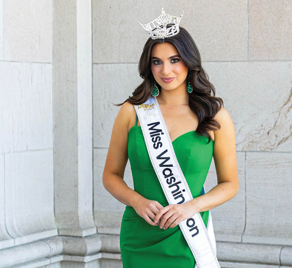 Мужчина опирается на кирпичную стену, за ним — дерево с вишневыми цветами.